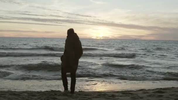 悲しい男海の海岸で、砂がスローされます。ビーチで波と夕日と海の美しい風景. — ストック動画