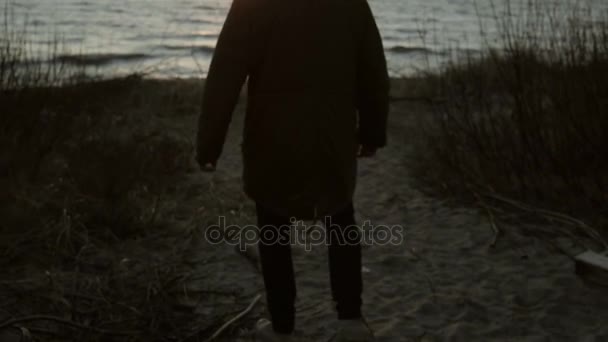 Jovem caminhando na praia de areia à noite. Triste masculino passar o tempo sozinho na costa da praia ao pôr do sol . — Vídeo de Stock