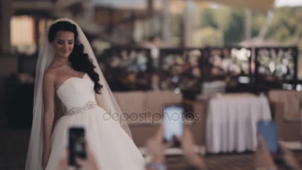 Krásná nevěsta pózuje během její přátelé fotografování na smartphone. Šťastná žena v bílých šatech ve svatební den. — Stock video