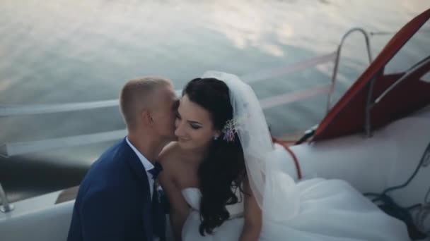 Happy newlyweds spending time on a sailboat in the open water together. Groom tenderly whispers in bride ear. — Stock Video