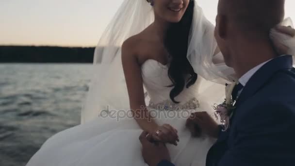 年轻美丽的新娘和新郎在风中航行。幸福的新婚夫妇坐在船上的游艇和谈日落. — 图库视频影像