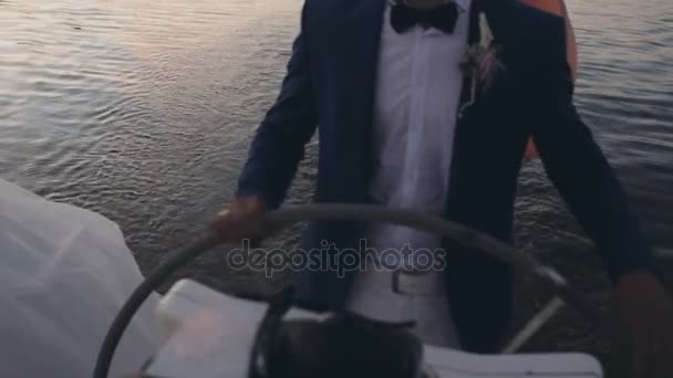 Empresario de traje de pie detrás de un volante en el velero. Joven marinero conduciendo el yate al atardecer . — Vídeo de stock