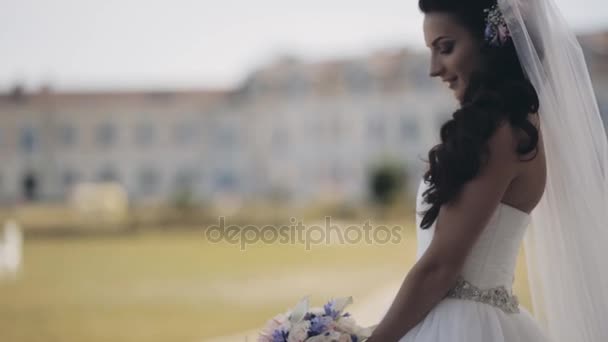 魅力的なブルネットの花嫁は結婚式のドレスを着て自然の中に立っています。美しい女性、花束を保持して式を待ちます. — ストック動画