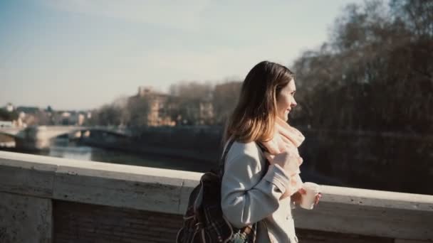 Jonge aantrekkelijke vrouw gaan aan het werk op de ochtend. Mooie vrouw op de brug van de stad wandelen en koffie drinken — Stockvideo