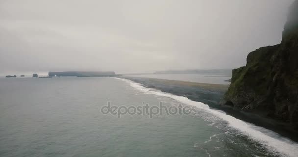 Αεροφωτογραφία του τη μαύρη ηφαιστειακή παραλία στην ομιχλώδη ημέρα. Πλήθος τουριστών περπατώντας στην ακτή της θάλασσας τέφρα. — Αρχείο Βίντεο