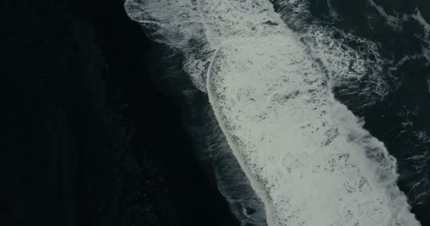 Luchtfoto bovenaanzicht van de krachtige golf met schuim komt op de kust van de zwarte vulkanische strand in IJsland. — Stockvideo