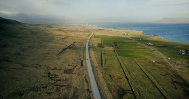 Aerial view of the scenic mountains road. Cars riding through the green field on the motorway near the shore of the sea. — Stock Video