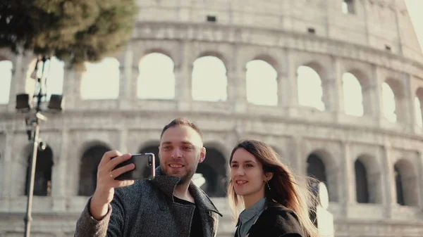 Young happy couple traveling in Rome, Italy. Man and woman taking the selfie photo on smartphone near the Colosseum.