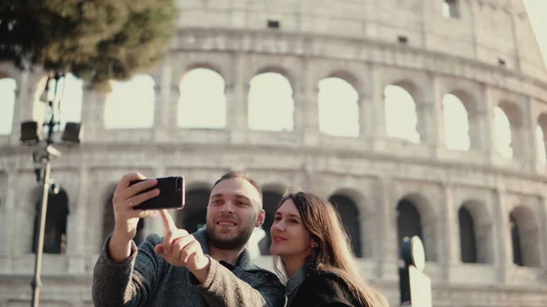 Felice giovane coppia utilizzando smartphone per scattare foto selfie vicino Colosseo a Roma, Italia. Uomo e donna hanno una vacanza . — Foto Stock