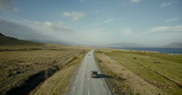 Vista aérea del camino de las montañas. Coches a caballo a través del campo verde en la autopista cerca de la orilla del mar . — Vídeos de Stock