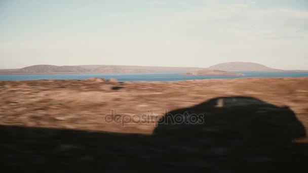 Blick im Auto auf wunderschöne Sonnenuntergangslandschaft mit Bergen und Wasser, See. Blick auf den Fahrzeugschatten von außen. — Stockvideo