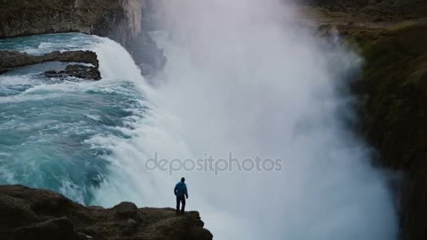 Paisaje escénico del hombre solitario de pie en el borde de la montaña y mirando la cascada Gullfoss en Islandia — Vídeos de Stock