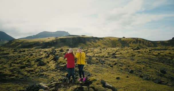 アイスランドの溶岩のフィールドの 2 つの女性の空撮は、手を上げてください。観光客を送るヘリコプター空気キスが幸せ. — ストック動画