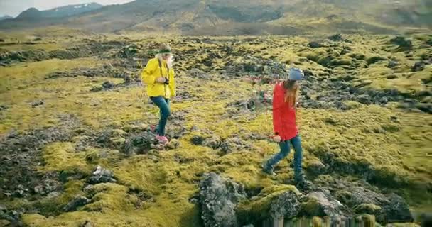 Copter voando em torno de duas mulheres no campo de lava na Islândia. Turistas com câmera andando na natureza e tirando fotos . — Vídeo de Stock