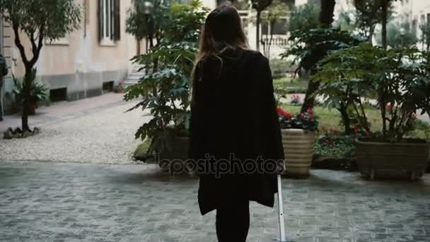 Rückansicht der jungen attraktiven Frau mit Koffer, die auf der Straße läuft. Frauen in Schwarz kommen in neue Stadt — Stockvideo