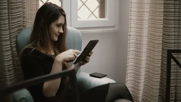 Junge schöne Frau sitzt zu Hause auf dem Stuhl und nutzt intelligente Technologien, arbeitet am Tablet-Computer. — Stockvideo