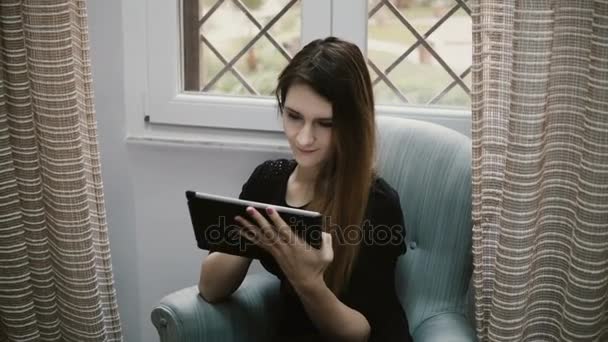 Joven hermosa chica morena navegar por Internet y el uso de la tableta de ordenador para eso. Chica atractiva descansando en casa . — Vídeos de Stock
