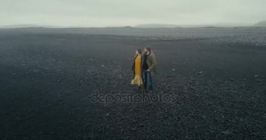 İzlanda'daki siyah volkanik sahilde yürüyen genç hippi çift hava görünümünü. Erkek ve kadın doğanın keyfini.