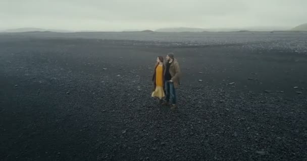 A légi felvétel a csípő fiatal pár séta a fekete vulkáni beach, Izland. Férfi és nő élvezi a természet. — Stock videók