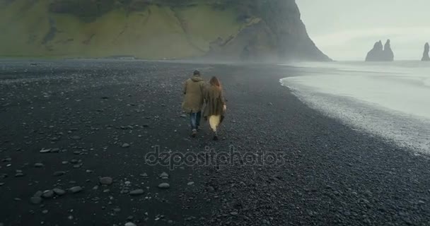 Назад пташиного польоту молодих hipster пара працює на чорний вулканічних пляж біля троль пальці в Ісландії. — стокове відео