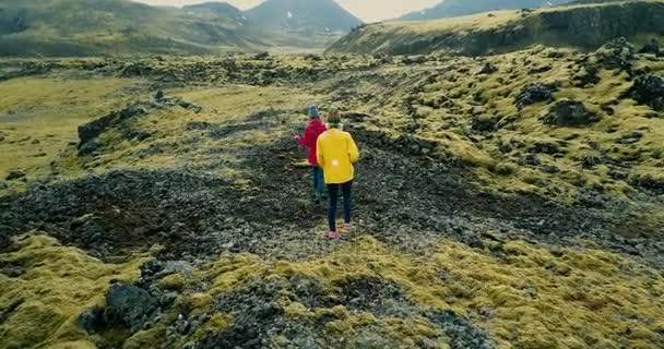 溶岩のフィールド上を歩いて 2 つの女性の空撮では、アイスランドのコケ覆われています。領土を探索する観光客. — ストック動画