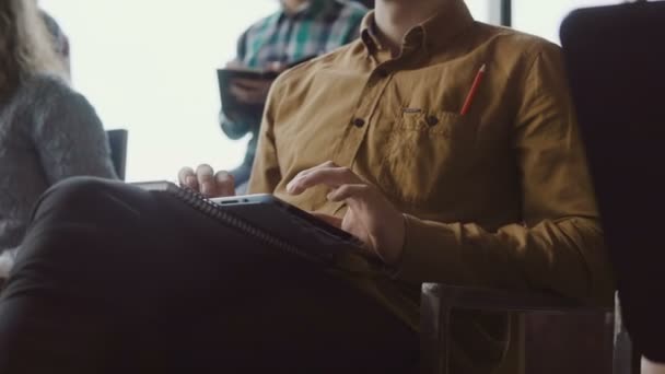 Vista de cerca del joven empresario sentado en el seminario y tomando notas en la tableta. Hombre en la oficina loft con el equipo joven . — Vídeo de stock