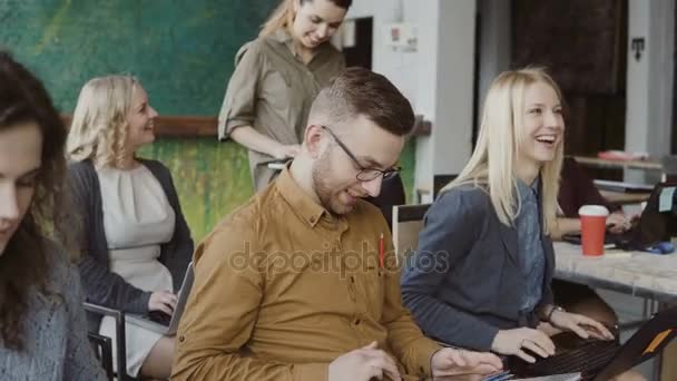 Young business team at modern office listening the training. Man and woman with laptop, tablet laugh and makes notes. — Stock Video