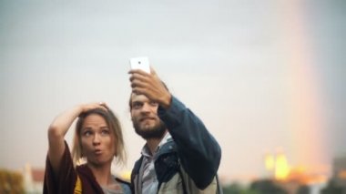 Genç çift selfie çekim gökkuşağı ile arka plan üzerinde. Neşeli adam ve kadın smartphone teknolojisini kullanır.