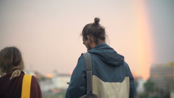 Joven pareja hipster caminando por la noche juntos. Hombre y mujer disfrutando de la puesta de sol, tomando fotos en el teléfono inteligente . — Vídeo de stock