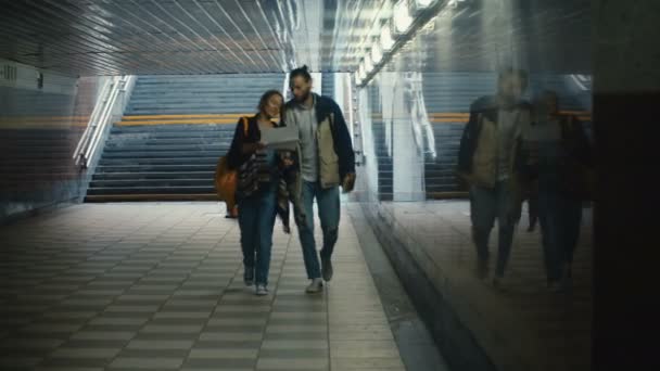 Νεαρό ζευγάρι ευτυχισμένο περπατώντας μέσα από το υπόγειο πέρασμα και ψάχνει στο χάρτη. Όμορφη τουρίστες στην πόλη της νέας. — Αρχείο Βίντεο