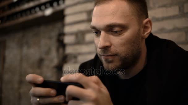 Retrato de un joven guapo sentado en el centro de la ciudad por la noche y usando el smartphone con pantalla táctil . — Vídeo de stock