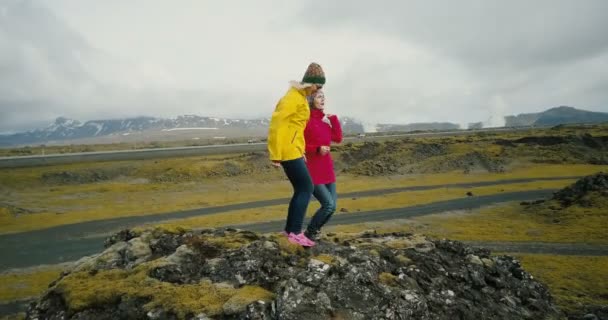 Vista aérea de los amigos parados en la cima de la montaña y bailando de felicidad. Dos mujeres en el campo de lava en Islandia . — Vídeo de stock