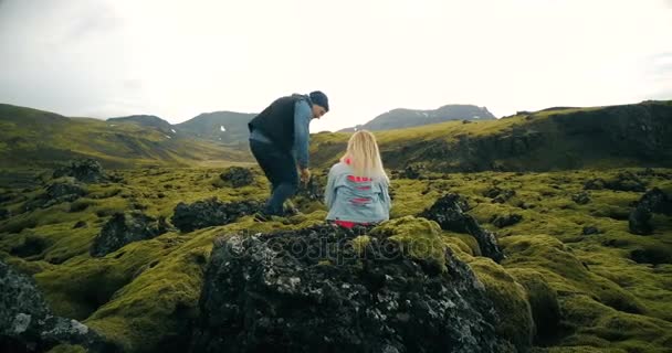 Achteraanzicht van jonge mooie paar zittend op de rots en genieten van het schilderachtige landschap van de lava velden in IJsland. — Stockvideo