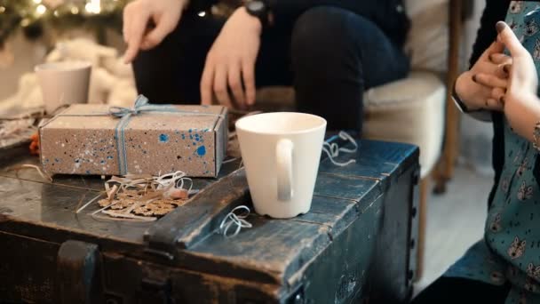 Close-up beeld van jonge paar zitten aan de tafel, het drinken van thee en het geven van Kerst presenteert aan elkaars. — Stockvideo