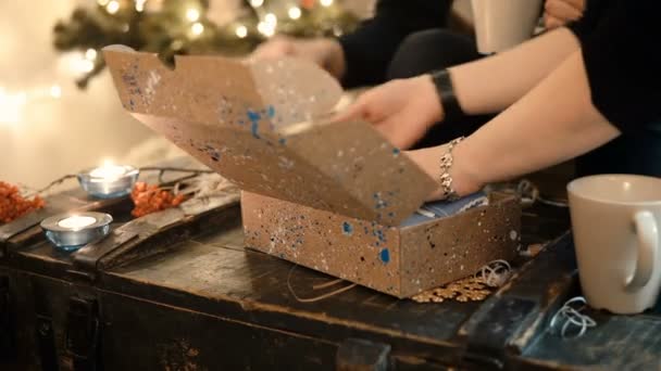 Jeune couple assis à la table et emballant des cadeaux de Noël à des amis, ambiance Nouvel An le soir . — Video