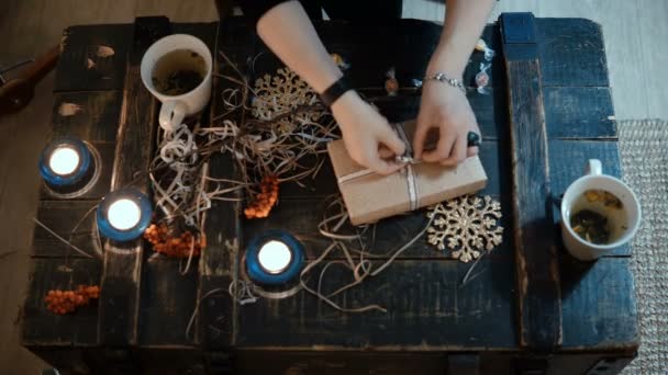 Vista superior de las manos femeninas empacando un regalo de vacaciones para amigos. Mujer joven decorando la caja de Navidad por la noche . — Vídeos de Stock