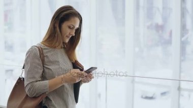 Genç güzel işkadını ofis binası içinde belgili tanımlık smartphone kullanarak. Meşgul erkek yürüyen merdiven iniyor.