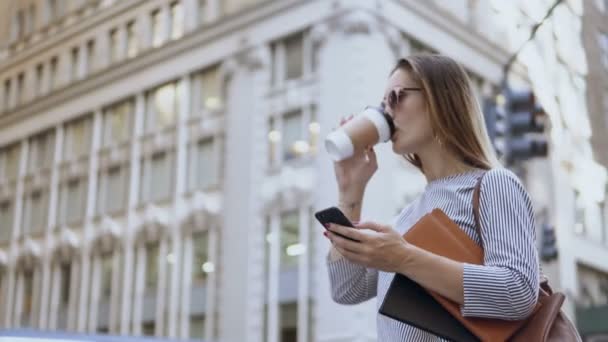 Joven mujer de negocios ocupada con gafas de sol sosteniendo los documentos, usando smartphone y tomando café en la calle . — Vídeos de Stock