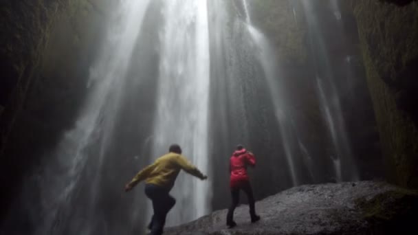 Young happy couple standing under beautiful waterfall Gljufrabui in Iceland and raises hands, feeling freedom and joy — Stock Video