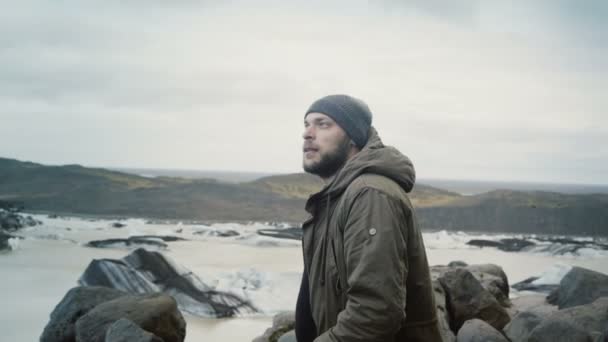 Ung resande man står på toppen av berget och tittar på glaciärer i Vatnajokull is lagunen på Island. — Stockvideo