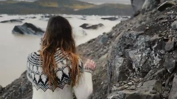 Vue arrière d'une jeune touriste marchant dans les montagnes à travers les rochers près de la lagune du glacier Vatnajokull en Islande . — Video