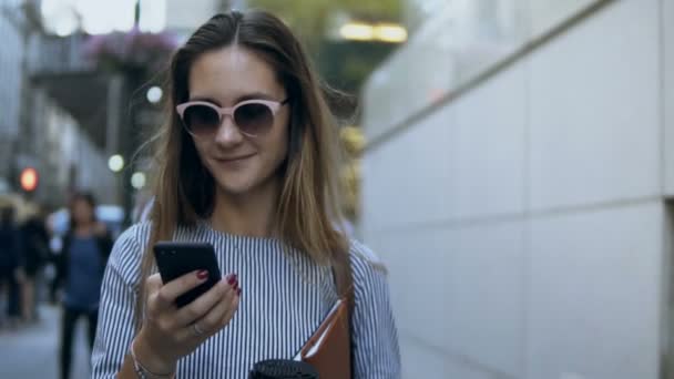 Retrato de una joven mujer de negocios hermosa caminando por la calle con documentos y café y usando un teléfono inteligente. Movimiento lento . — Vídeo de stock