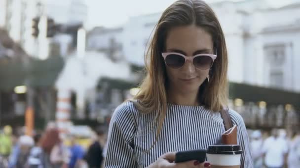 Retrato de la joven mujer de negocios hermosa de pie en la calle llena de gente sosteniendo el café y los documentos, utilizando el teléfono inteligente . — Vídeos de Stock