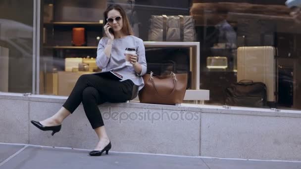 Pausa de café de mulher de negócios elegante jovem. Mulher feliz sentada perto da vitrine e usando smartphone, conversando . — Vídeo de Stock