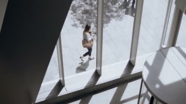Büyük pencerelerden binanın içinde görüntüleyin. Ofisler yürüyüş ve smartphone kullanarak genç meşgul kadın.