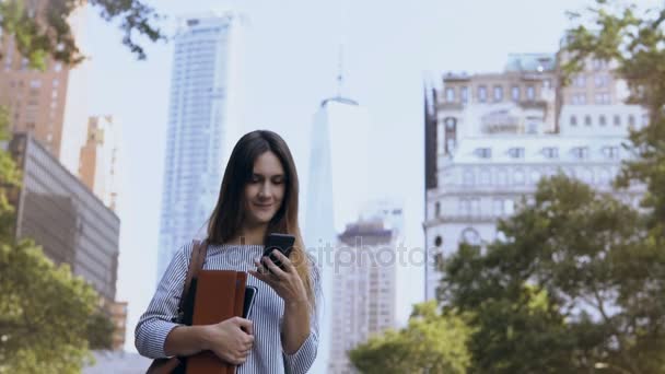 Retrato de jovem mulher de negócios feliz em pé perto do prédio de escritórios, detém notebooks e usar o smartphone . — Vídeo de Stock