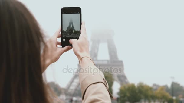 Jovem mulher bonita andando em Paris, França e tirando fotos da Torre Eiffel em neblina no smartphone ou telefone celular . — Vídeo de Stock