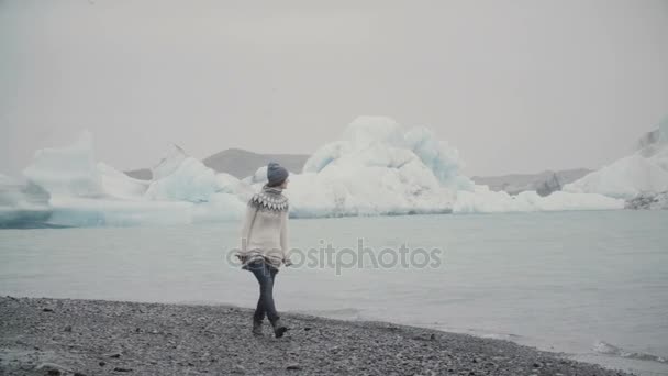 Νέα ελκυστική γυναίκα περπατώντας στην ακτή της λιμνοθάλασσας του πάγου. Τουριστικά, εξερευνώντας το περίφημο θέαμα με παγετώνες της Ισλανδίας. — Αρχείο Βίντεο