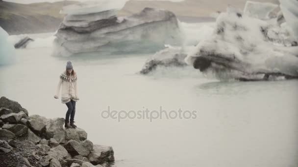 Young happy woman walking on the shore of ice lagoon. Tourist in lopapeysa exploring the sights of Iceland. — Stock Video