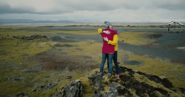 Vista aérea de las dos mujeres de pie en la cima de la montaña cubierto de musgo y abrazos. Turistas en campo de lava en Islandia — Vídeo de stock